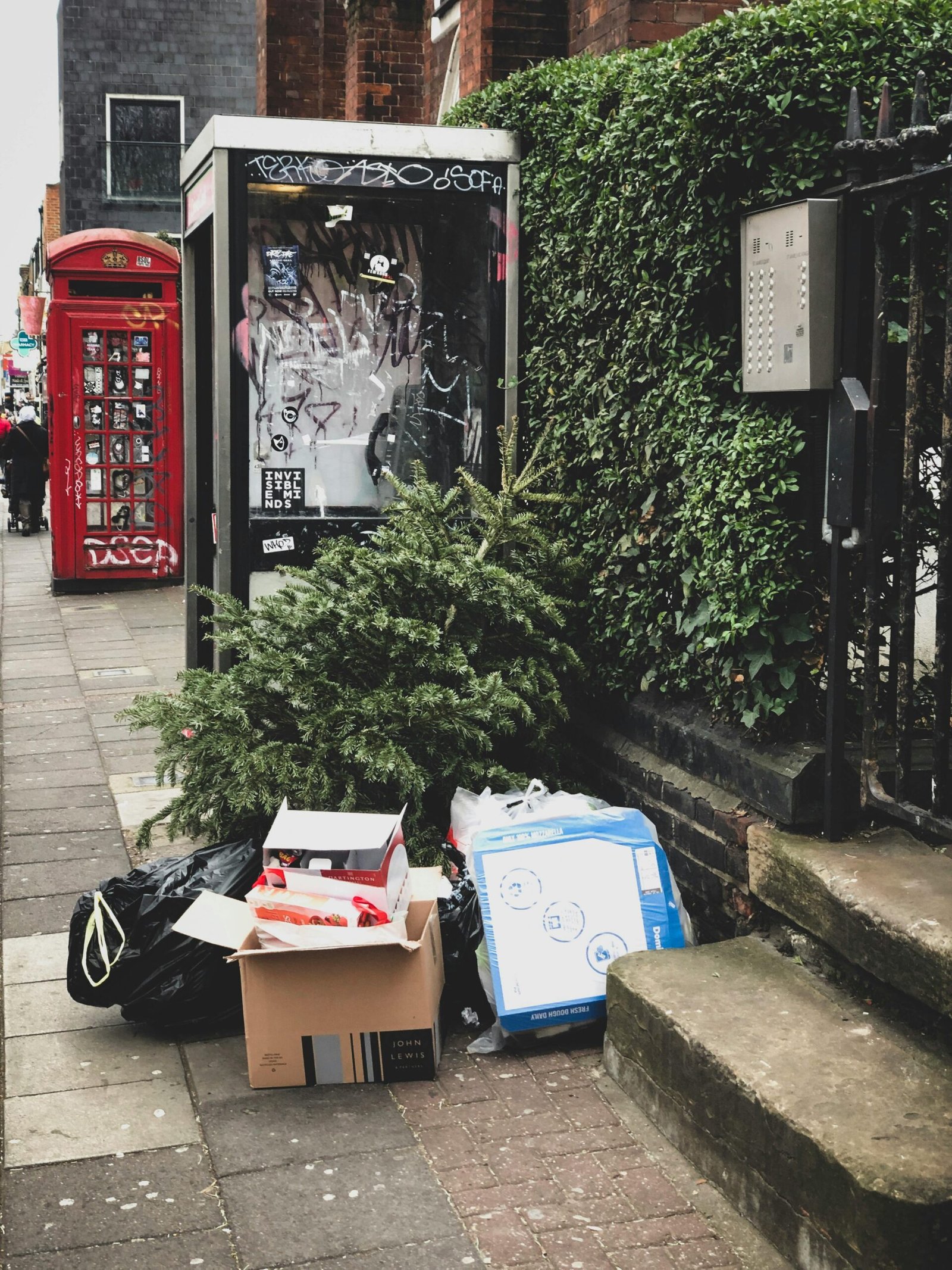 An abandoned Christmas tree with trash on a busy London sidewalk highlights post-holiday waste.