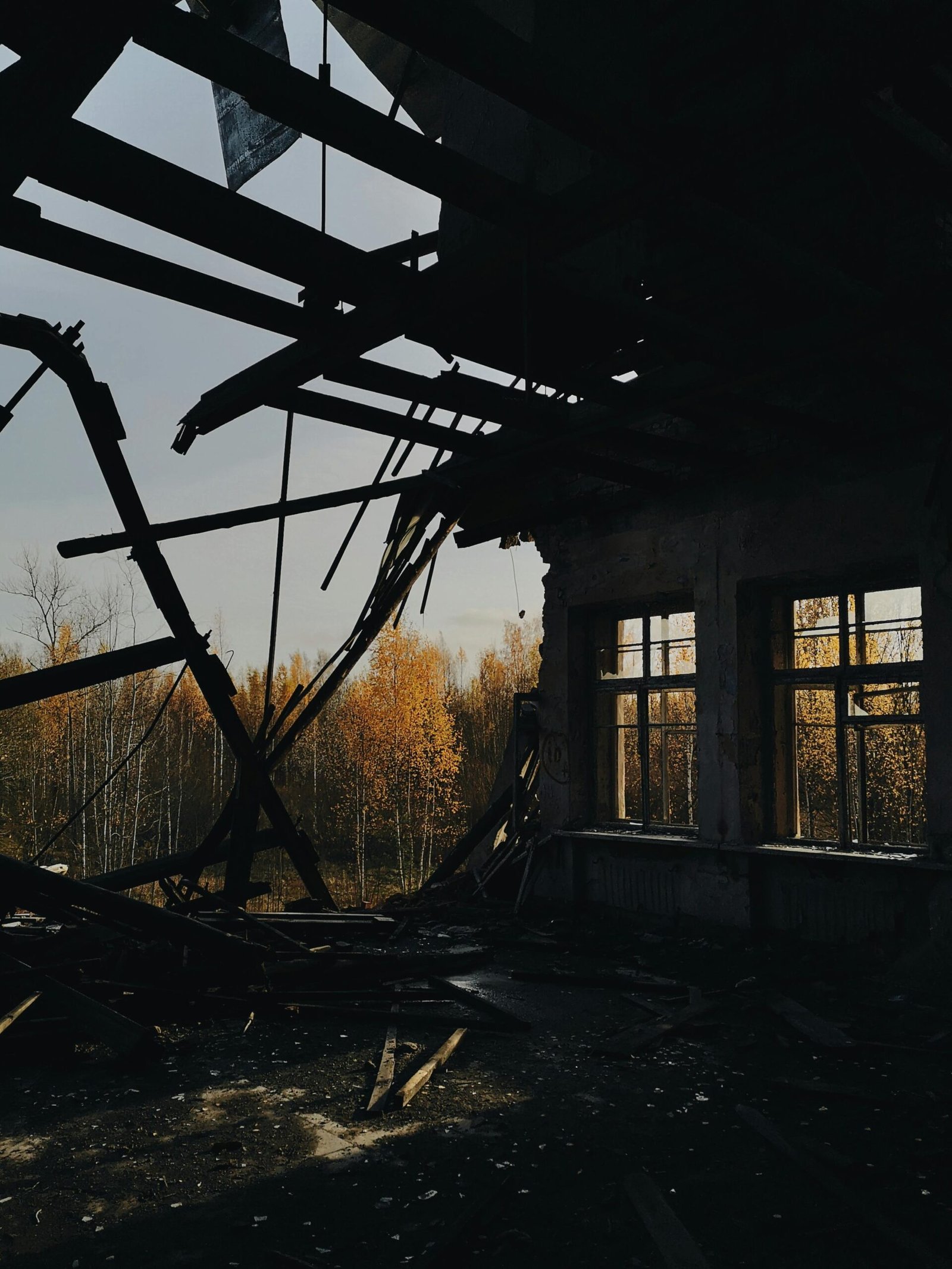 A captivating view through a decaying building's roof with autumn trees outside.