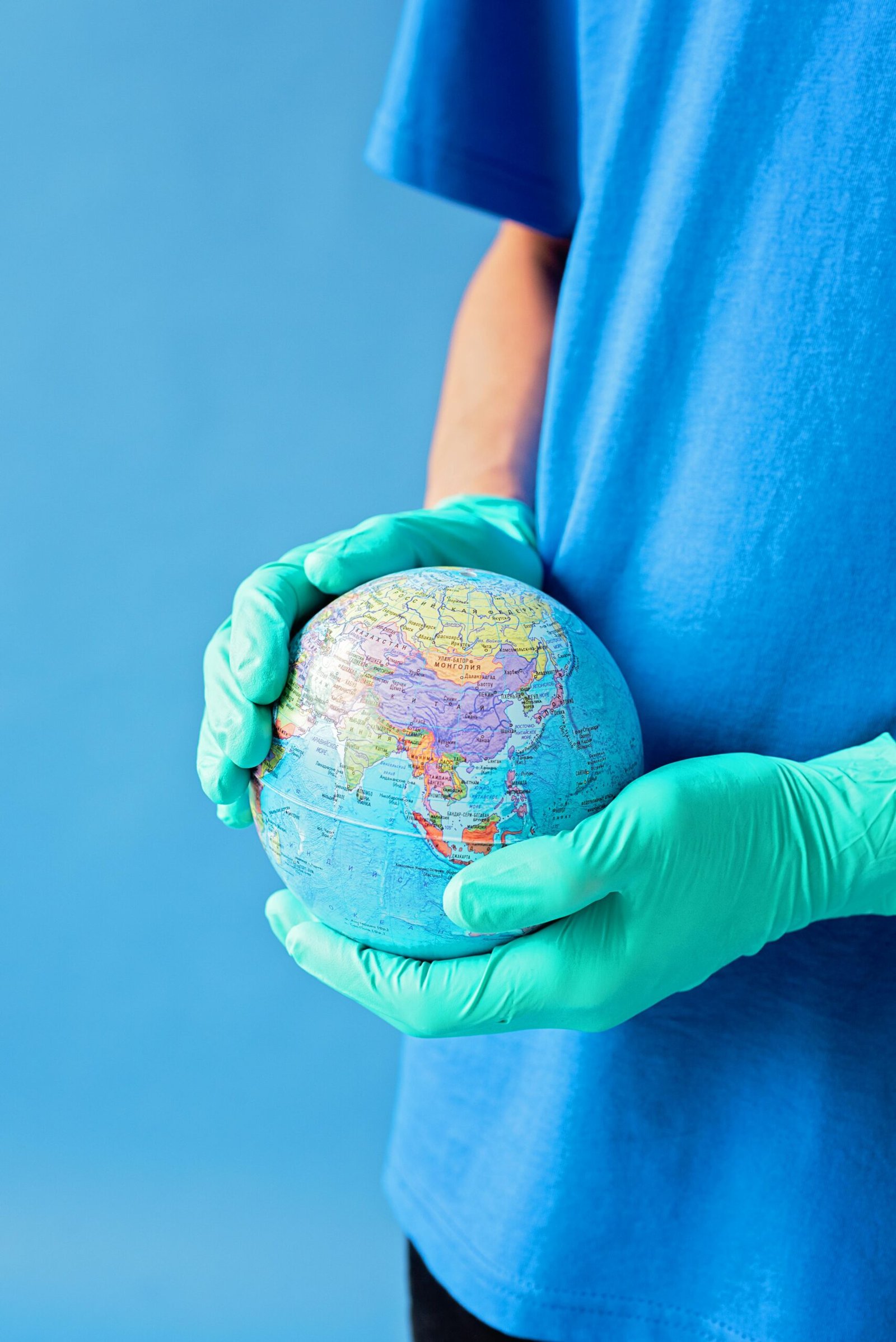 Person in gloves holds a globe against a blue background, symbolizing world protection.